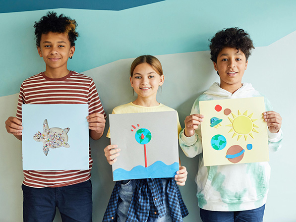 Three students holding up artwork
