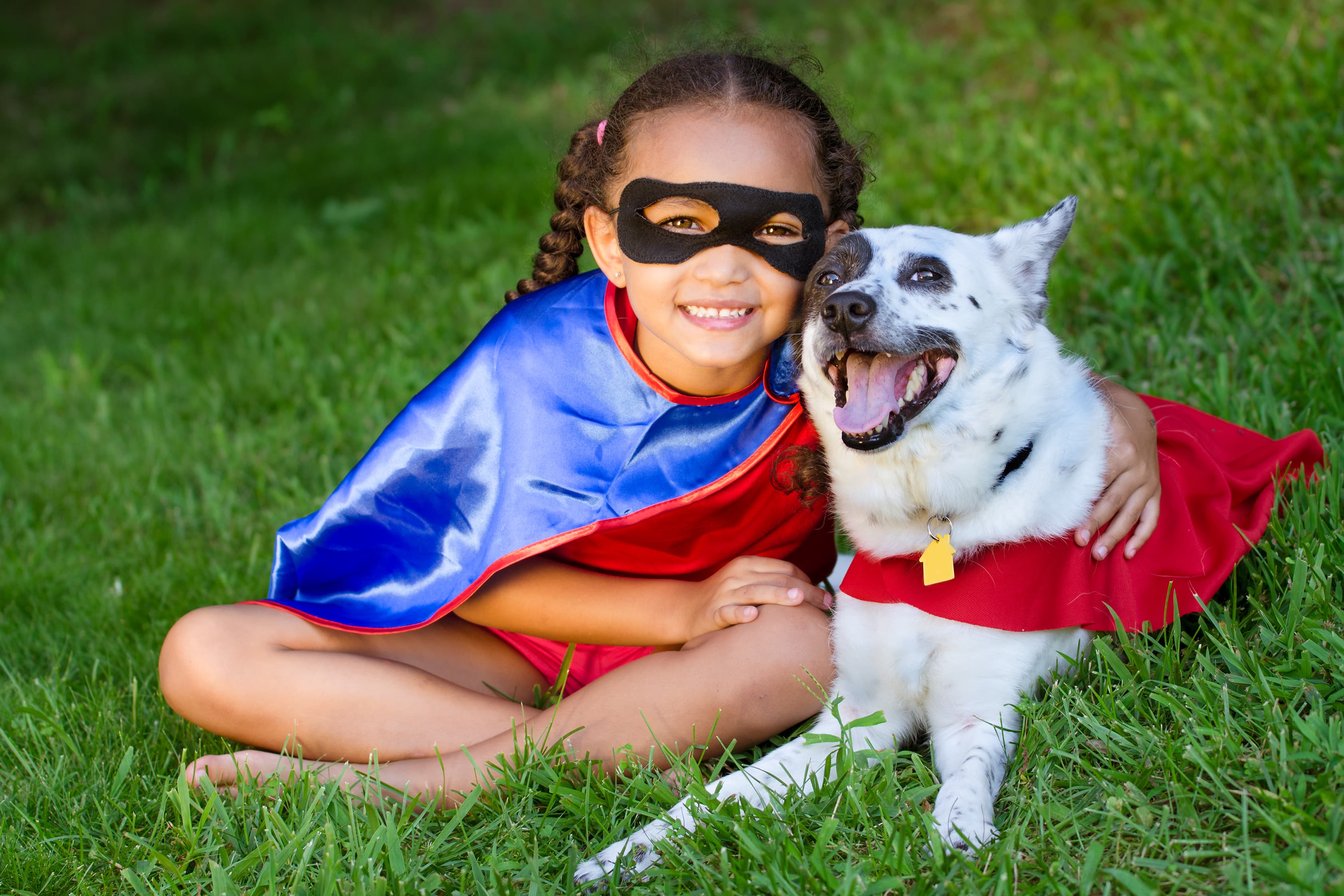child dressed as a superhero with arm around dog who is wearing a cape
