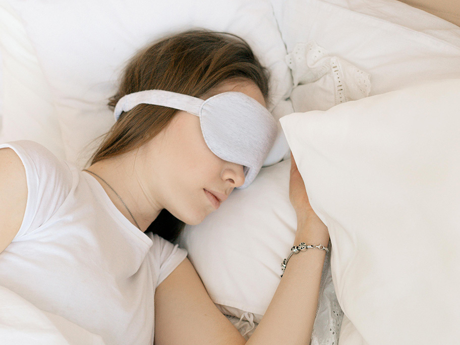 A woman with a mask over her eyes lays her head on a pillow
