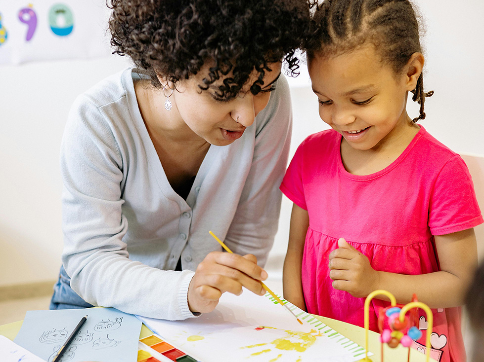 A teacher and preschool age student work on an art project at a table